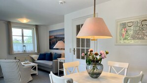 A room with a dining table, chairs, a sofa, a window, and a lamp.