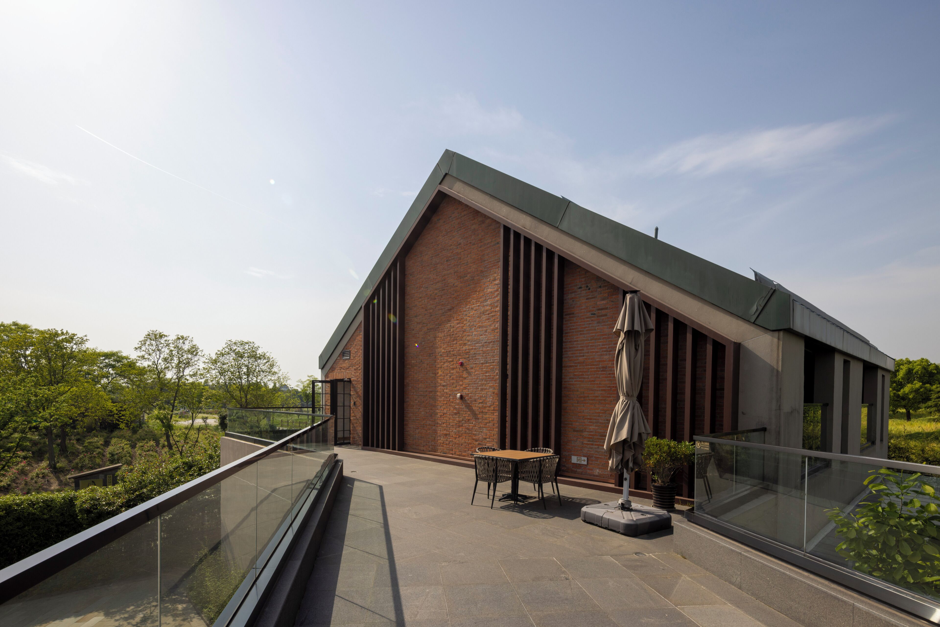 A modern building with a glass balcony, outdoor seating, and a brick facade.