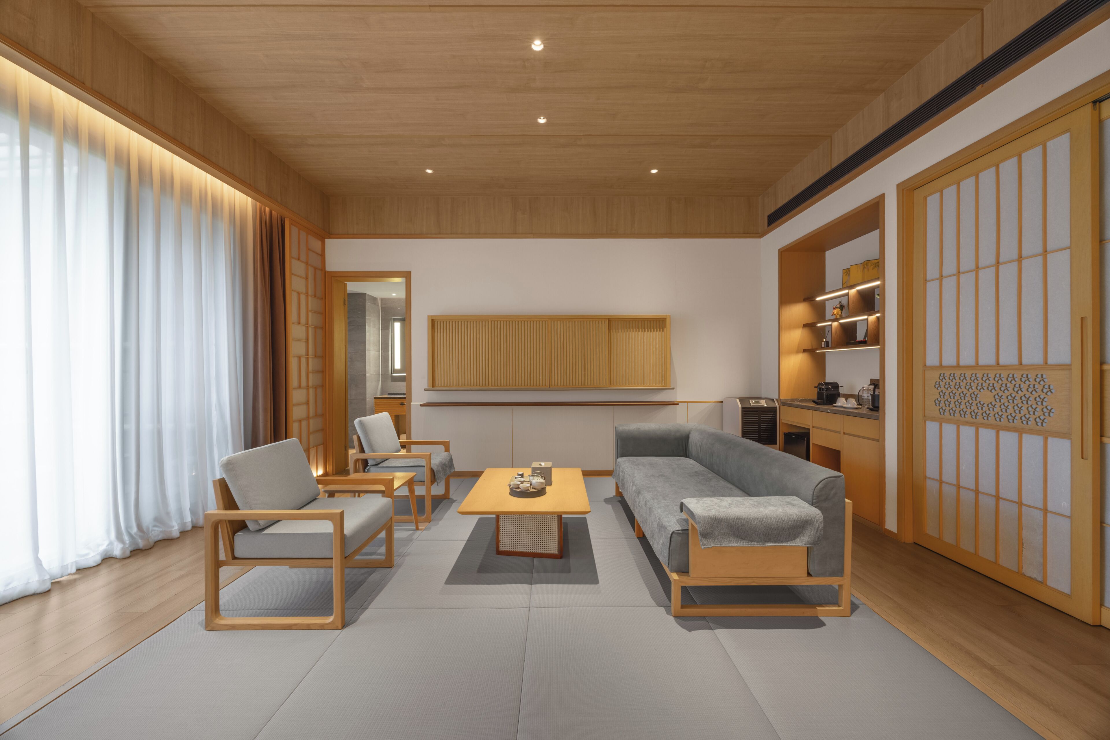 A modern living room with a sofa, chairs, a coffee table, wooden flooring, and a sliding door with a traditional design.
