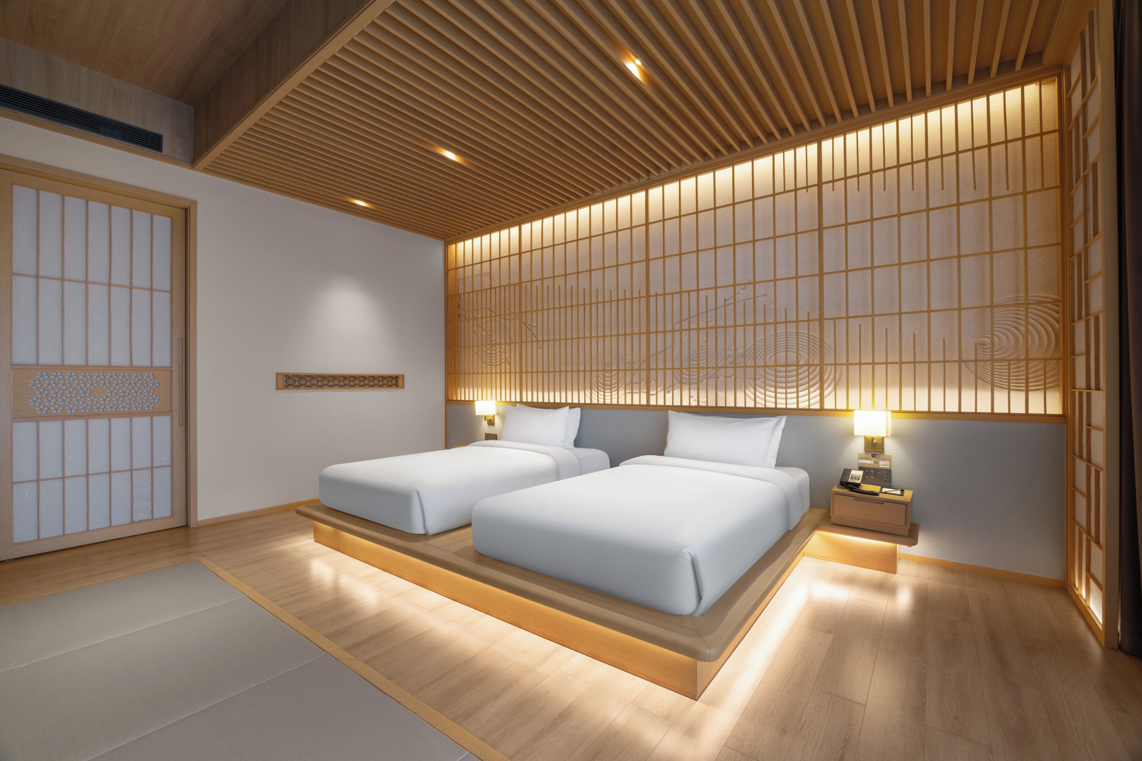 A hotel room with a traditional Japanese aesthetic, featuring a tatami mat floor, a low wooden ceiling, and a shoji screen wall.