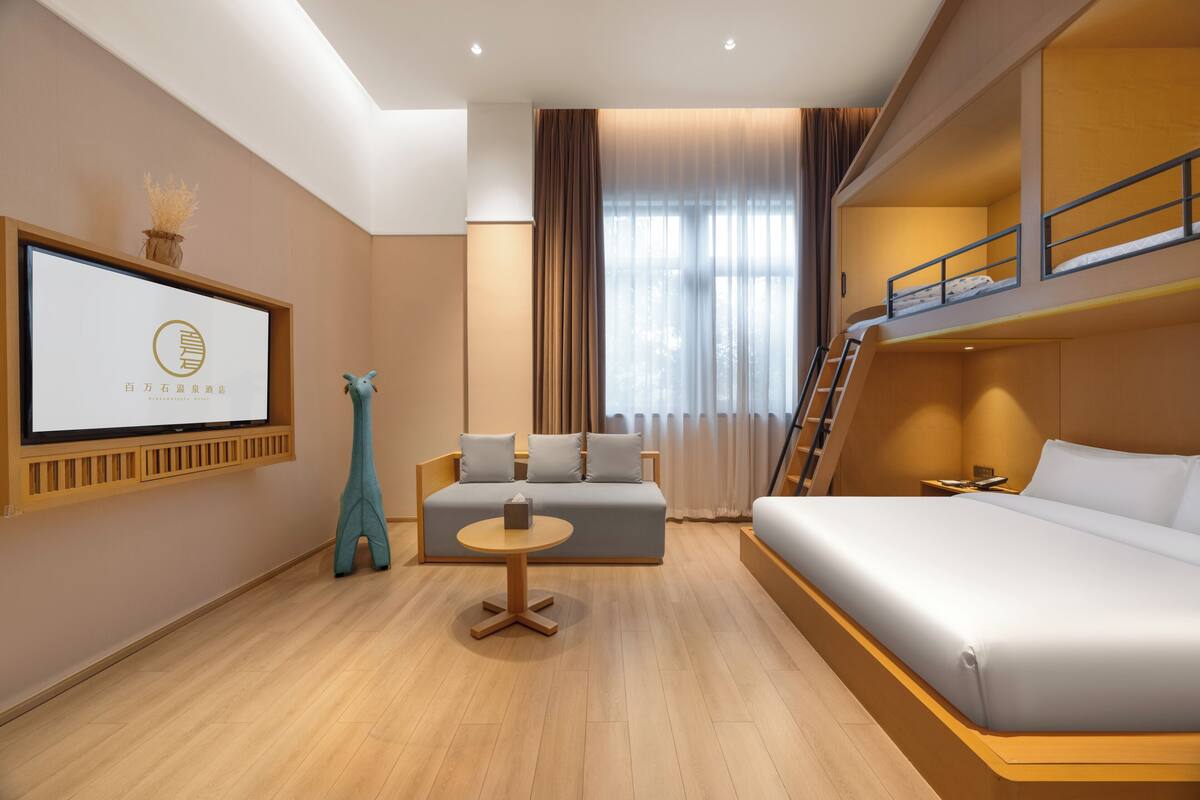 Une chambre d’hôtel moderne avec un canapé, une petite table ronde, un lit superposé et un tableau encadré au mur.