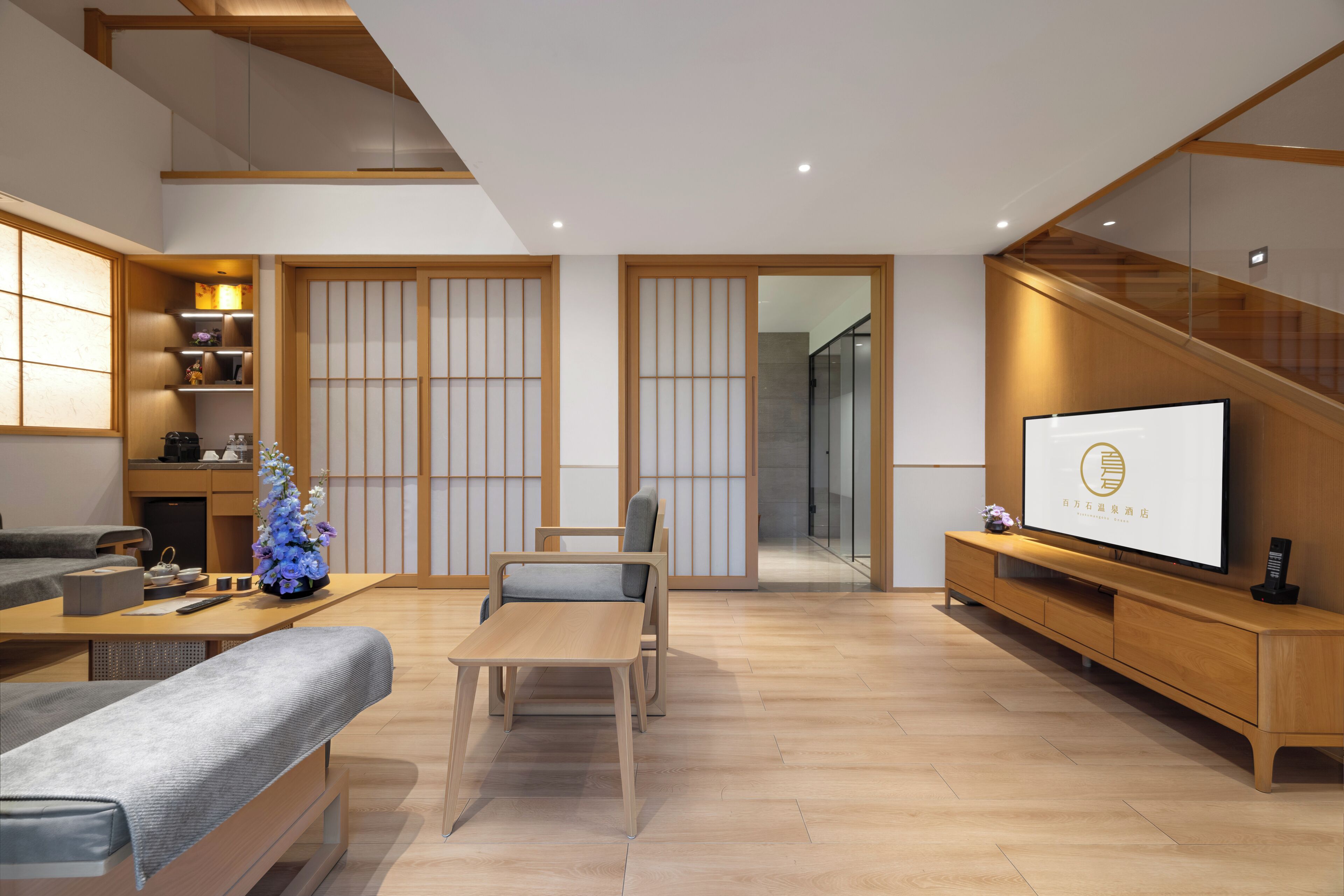 A modern living room with a sofa, a wooden coffee table, a TV on a wooden stand, and a staircase.