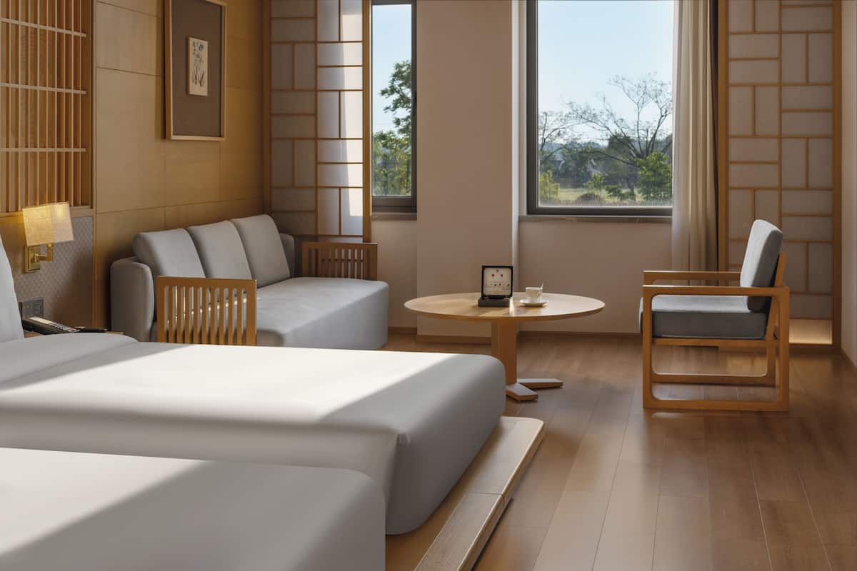Une chambre d’hôtel avec deux lits, un canapé, une chaise, une petite table et de grandes fenêtres donnant sur l’extérieur.