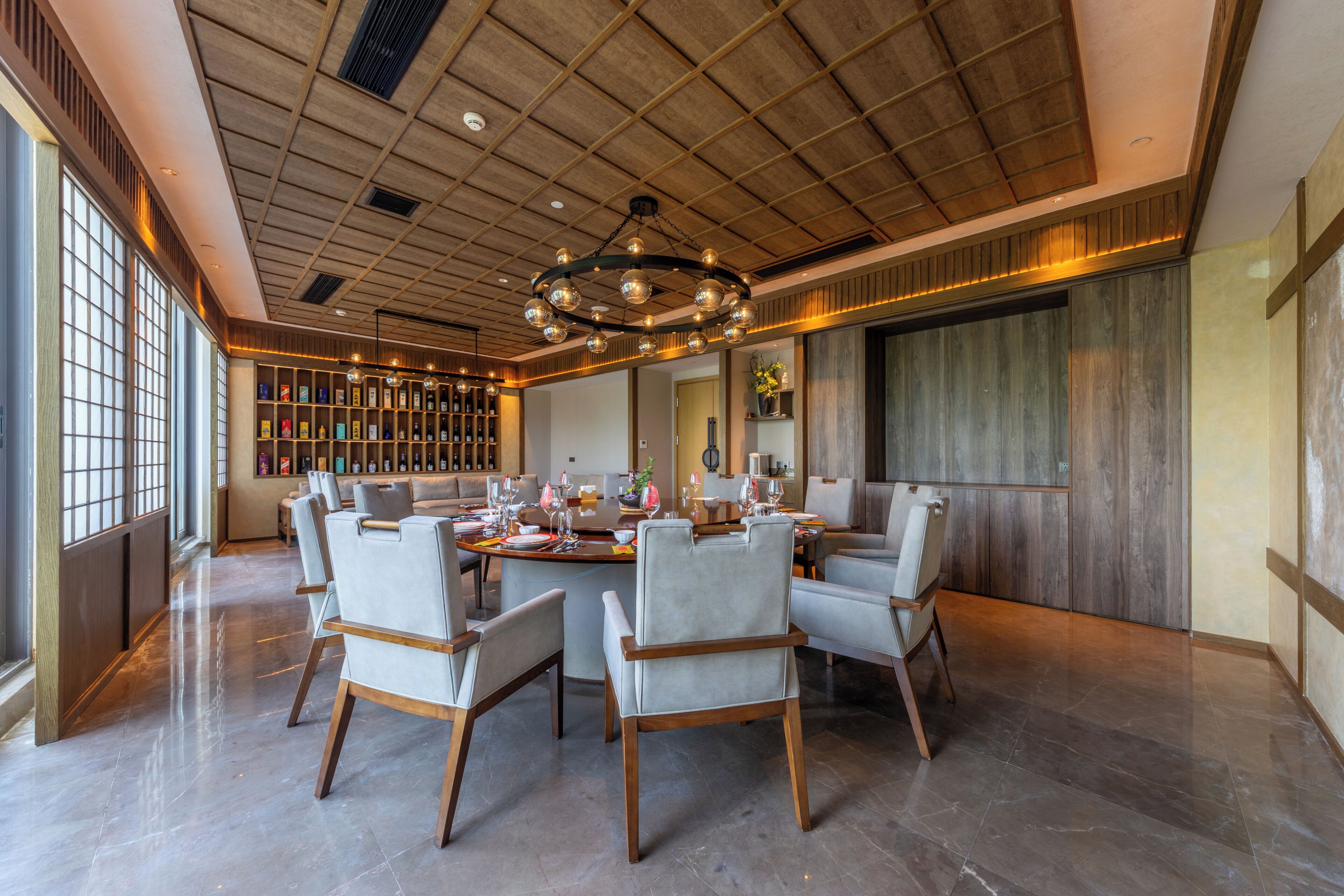 Uma ampla sala de jantar com mesa redonda, várias cadeiras e um grande lustre.