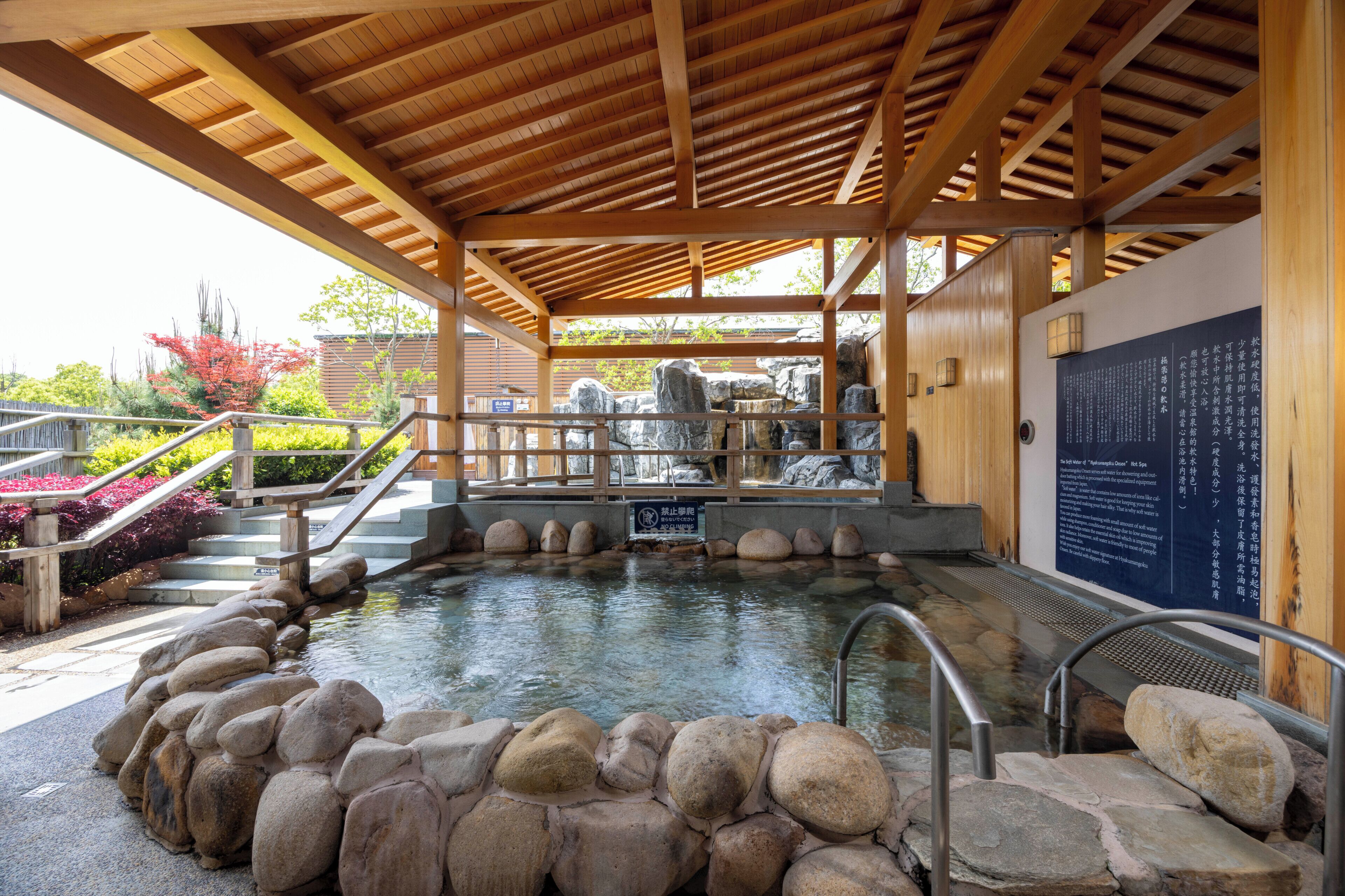 A traditional Japanese onsen with a wooden roof, stone steps, and a stone wall with inscriptions.