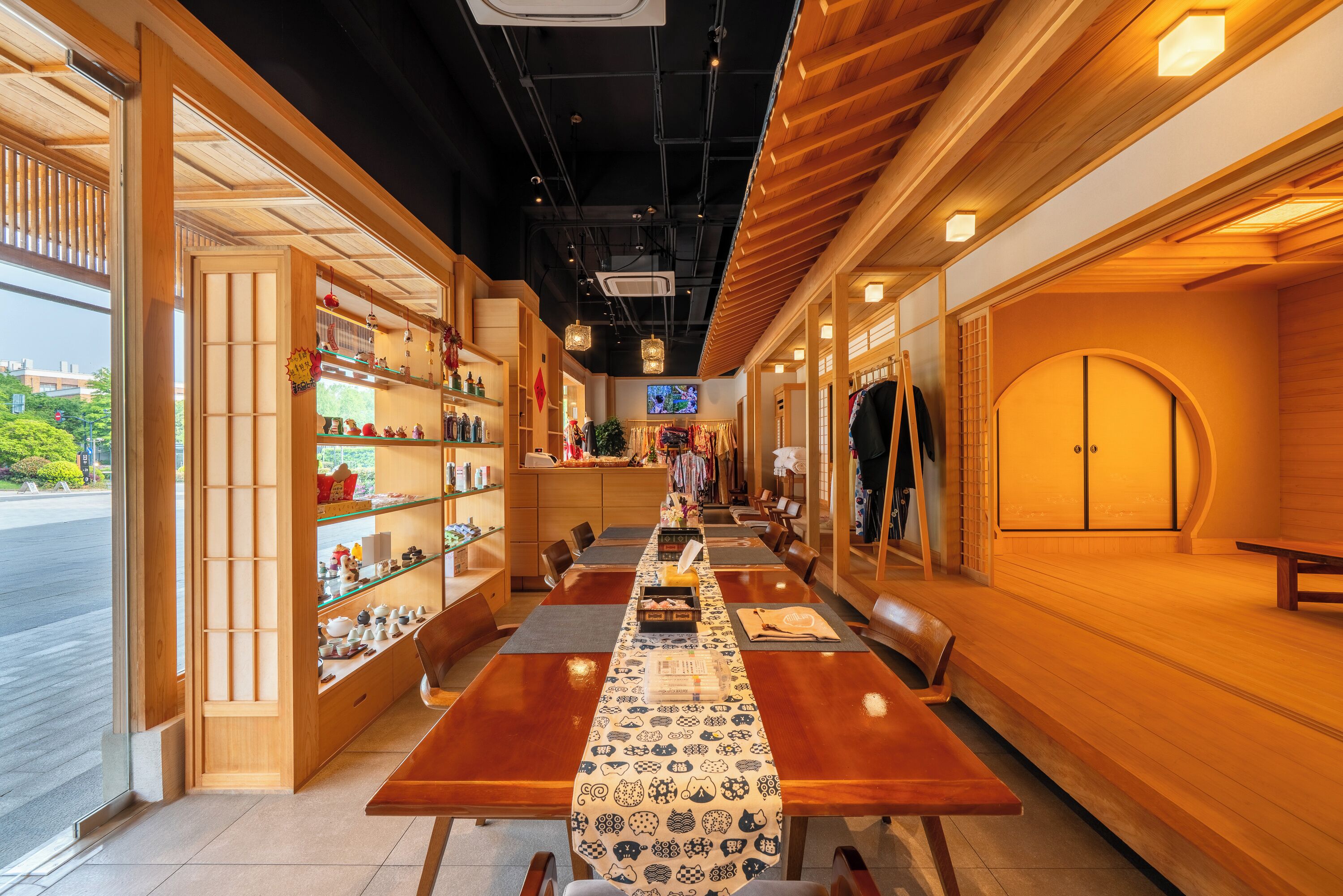 A restaurant with a long wooden table, shelves with bottles, and a TV screen.