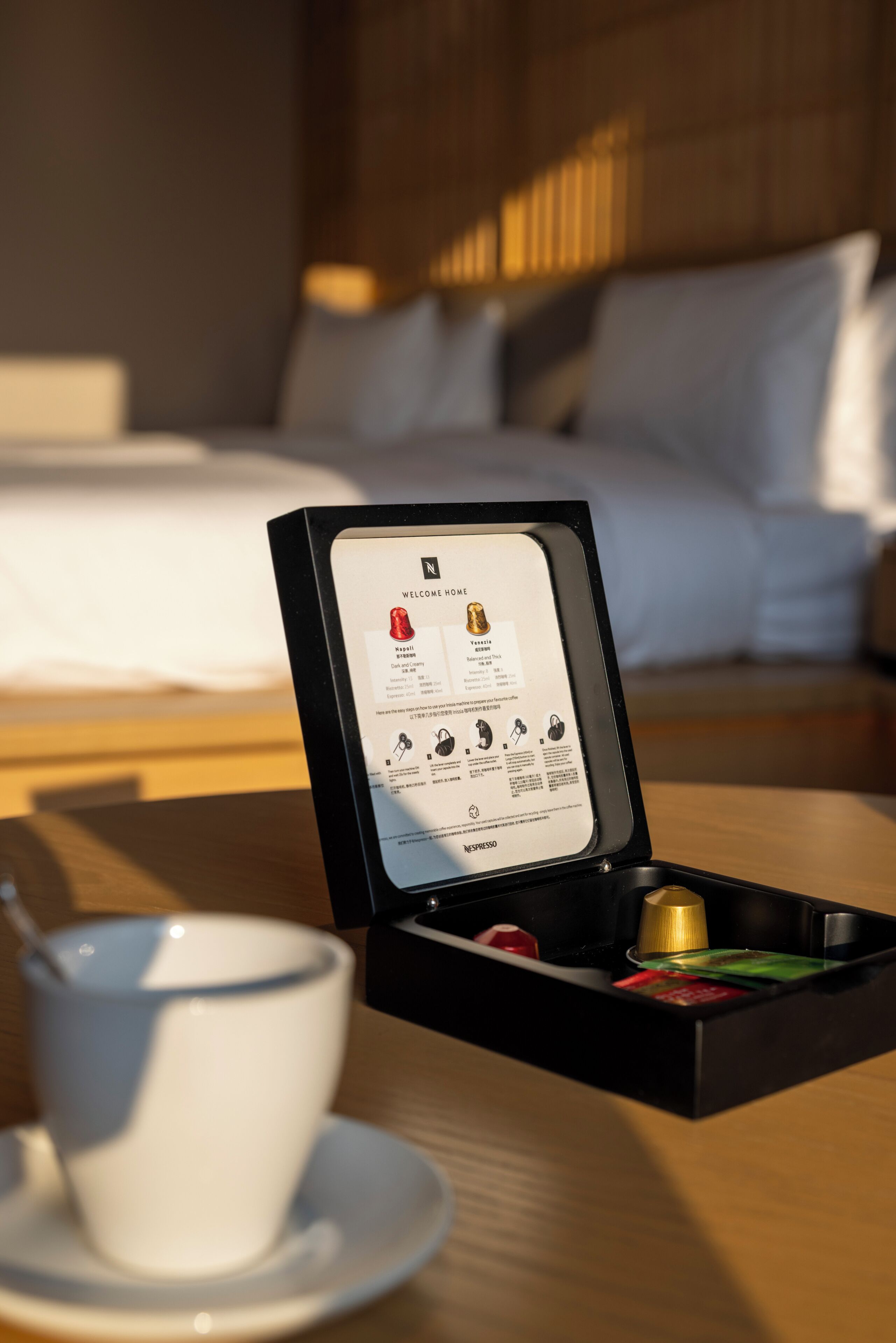 A neatly arranged tray with a cup and a box containing a tea set, placed on a wooden table in a hotel room.