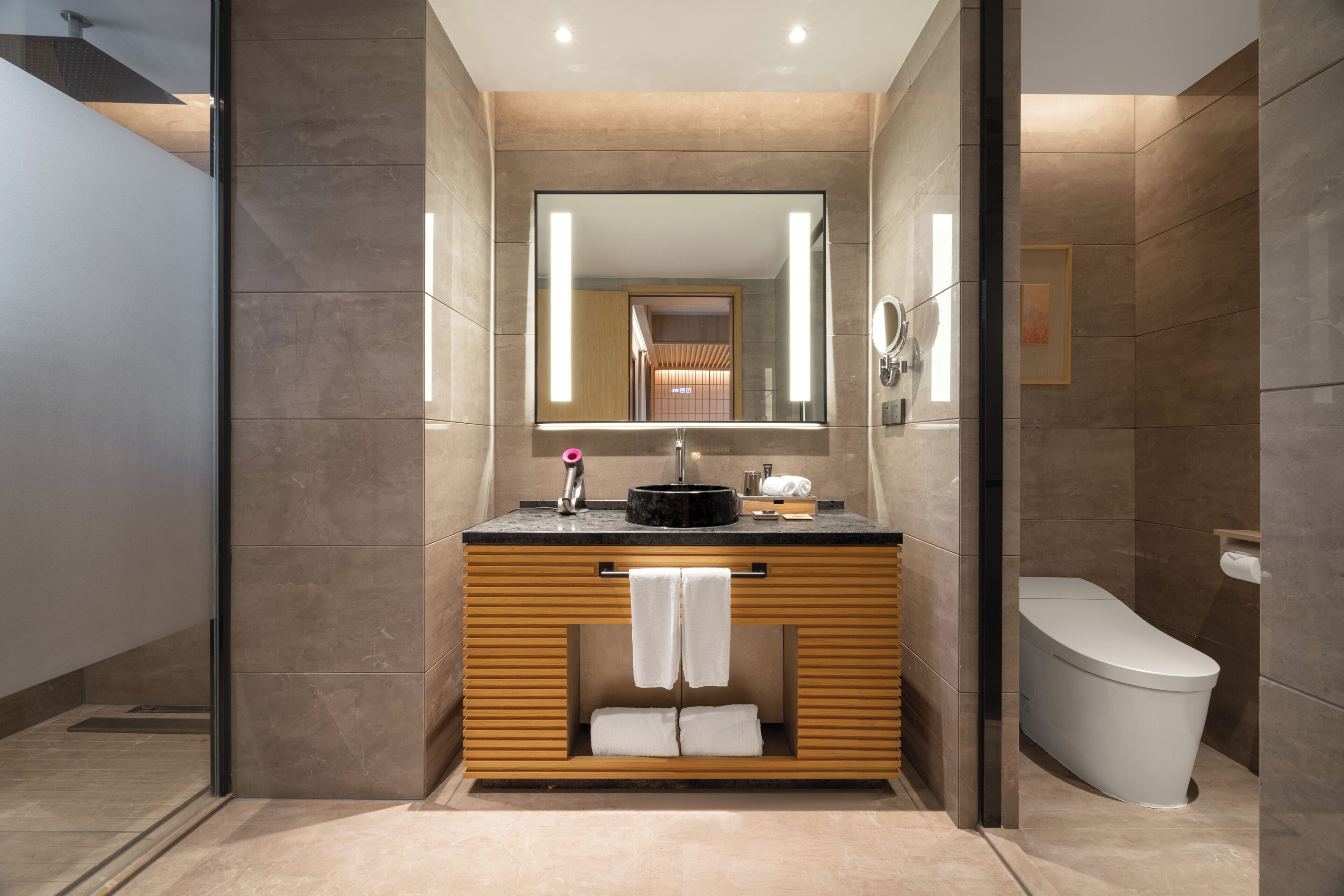 Une salle de bain moderne avec un meuble-lavabo en bois, un lavabo noir, un miroir et des toilettes.