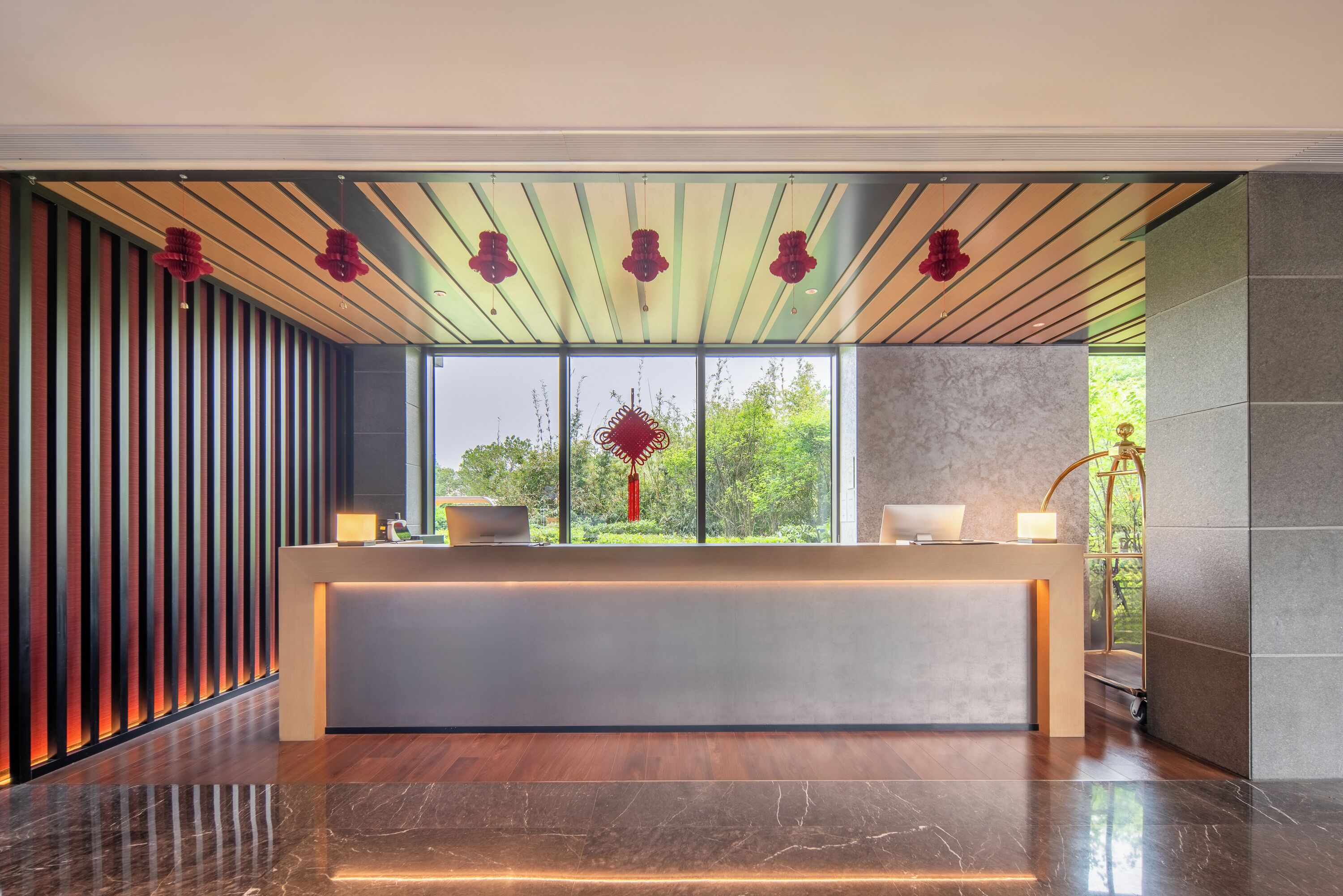 A reception desk with a modern design, large windows, and a view of greenery outside.