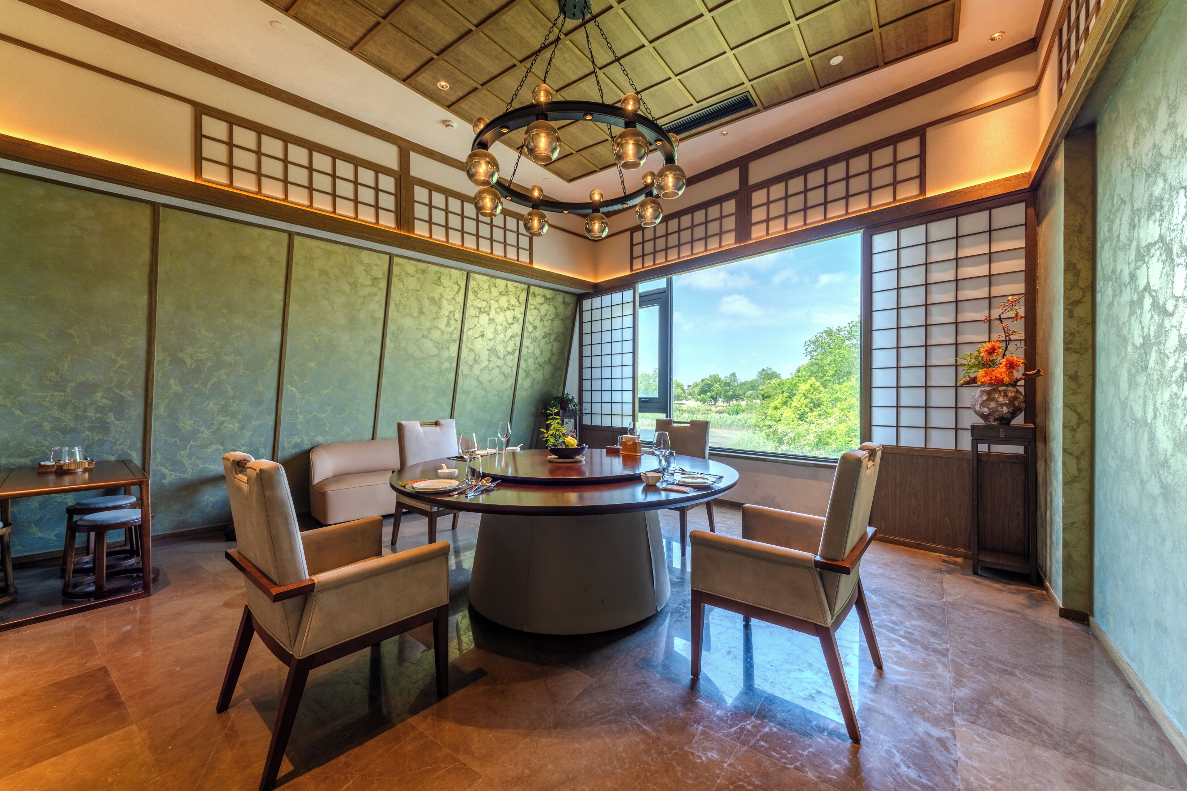 A traditional Japanese-style room with tatami flooring, a round table with chairs, a shoji screen, and a view of greenery outside.