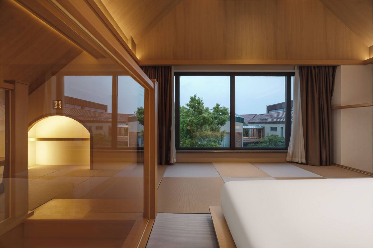 Une chambre d’hôtel avec des tatamis, une grande fenêtre avec des rideaux et une vue sur les bâtiments environnants.