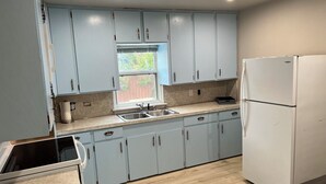 A kitchen with light blue cabinets, a double sink, a refrigerator, and a window with a view of greenery outside.