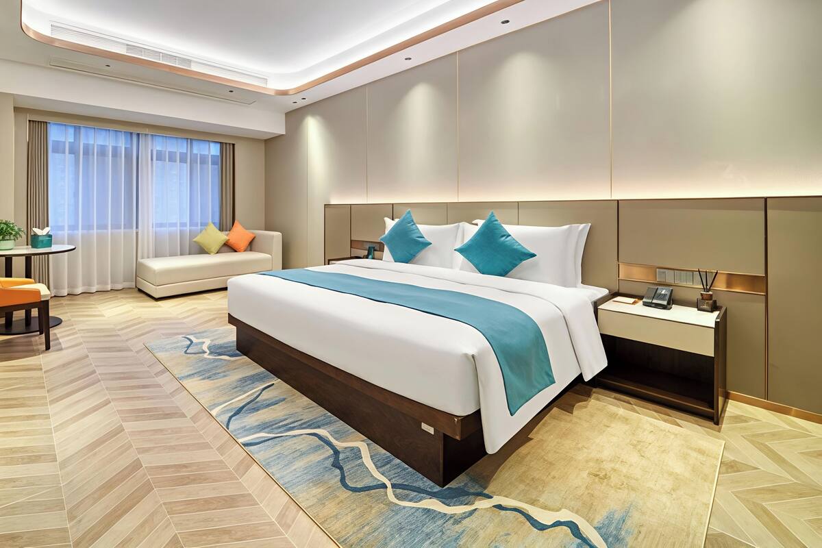 Una camera d'albergo moderna con un letto grande, un comodino con una lampada, un divano e un tavolino con una pianta.