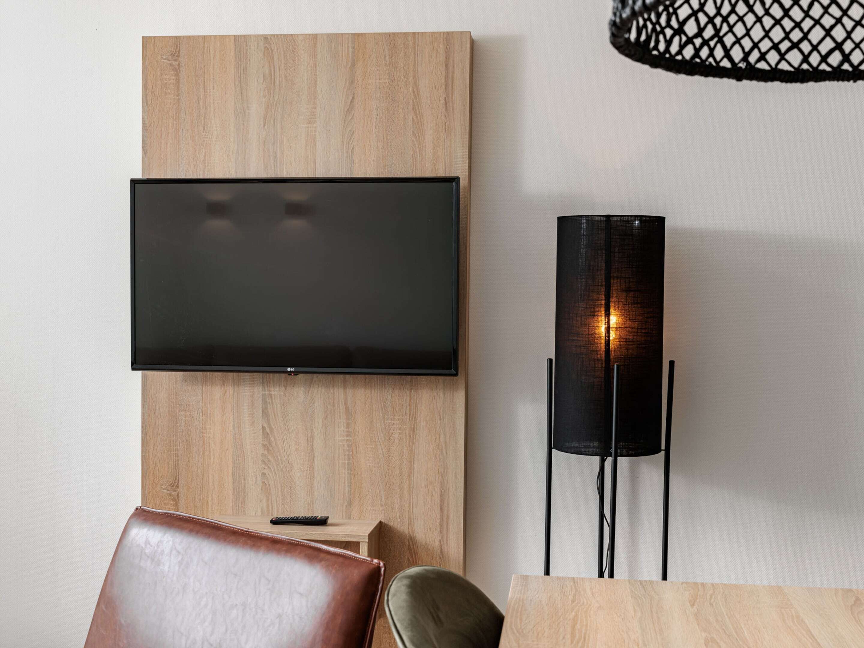 Uma sala de estar moderna com uma TV de tela plana fixada numa parede de madeira, um abajur de chão alto e um sofá de couro.