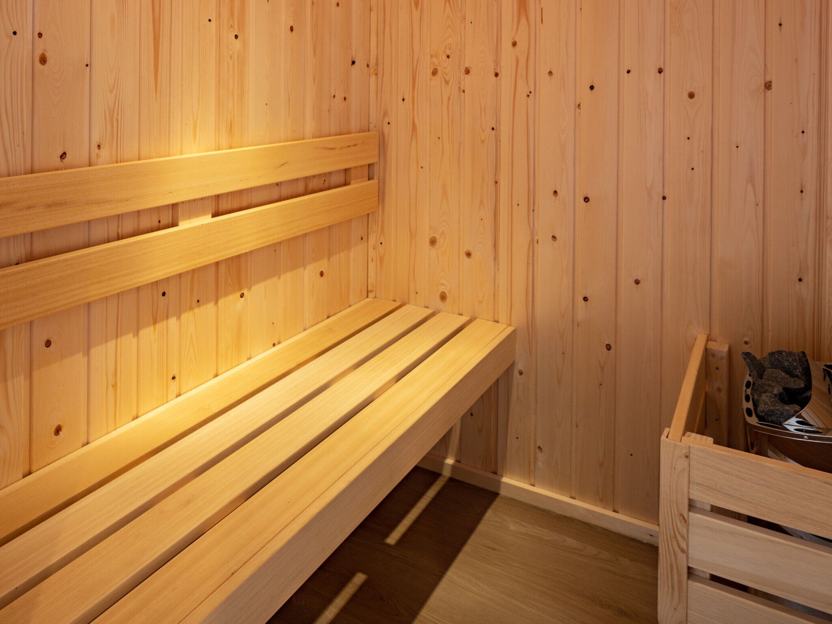 A wooden sauna bench with a slatted design, a wooden wall with evenly spaced holes, and a wooden bench with a curved backrest.