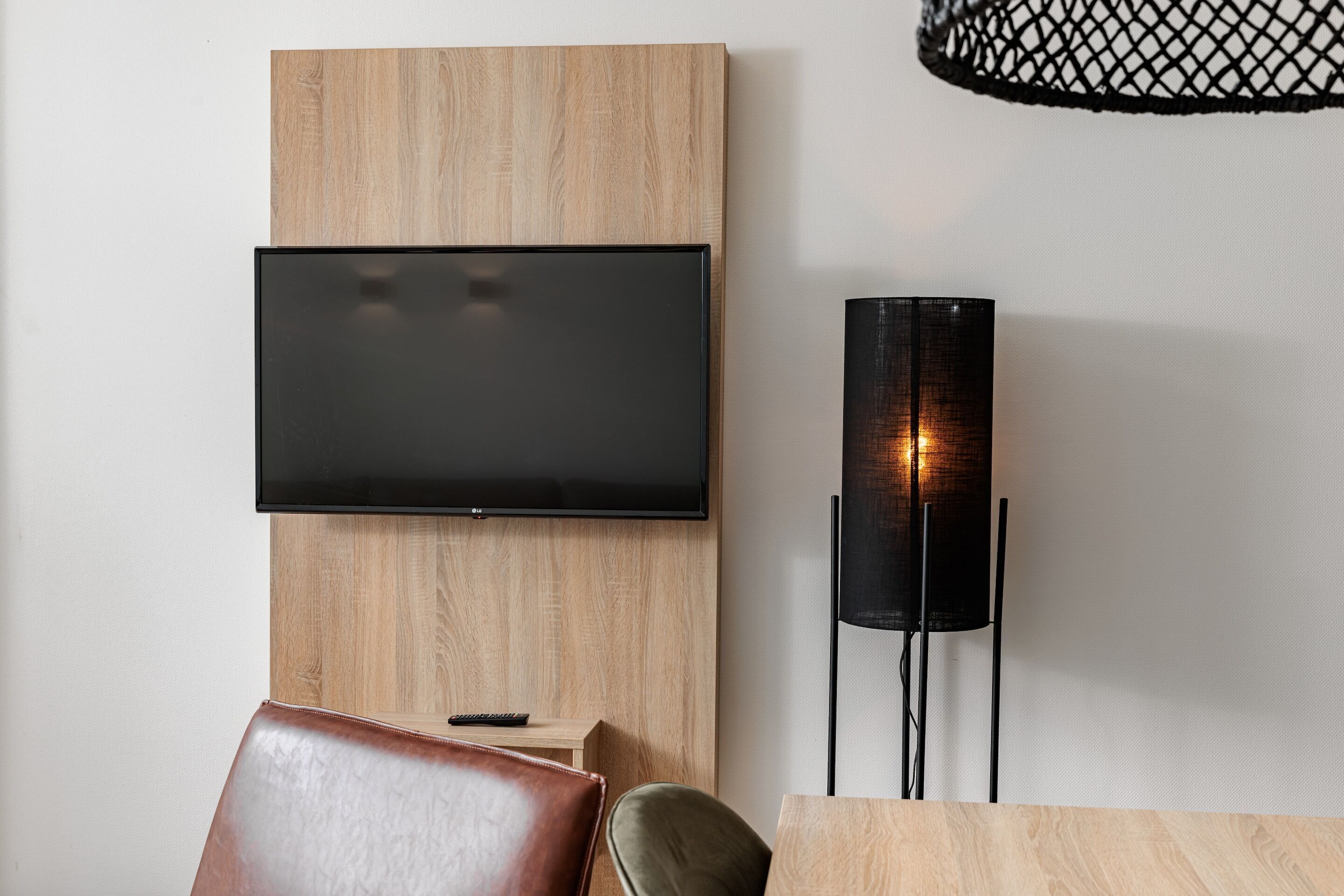 A modern living room with a mounted flat-screen TV, a tall floor lamp, a wooden accent wall, and leather seating.