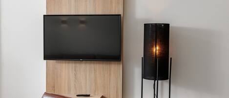A modern living room with a mounted flat-screen TV, a tall floor lamp, a wooden accent wall, and leather seating.