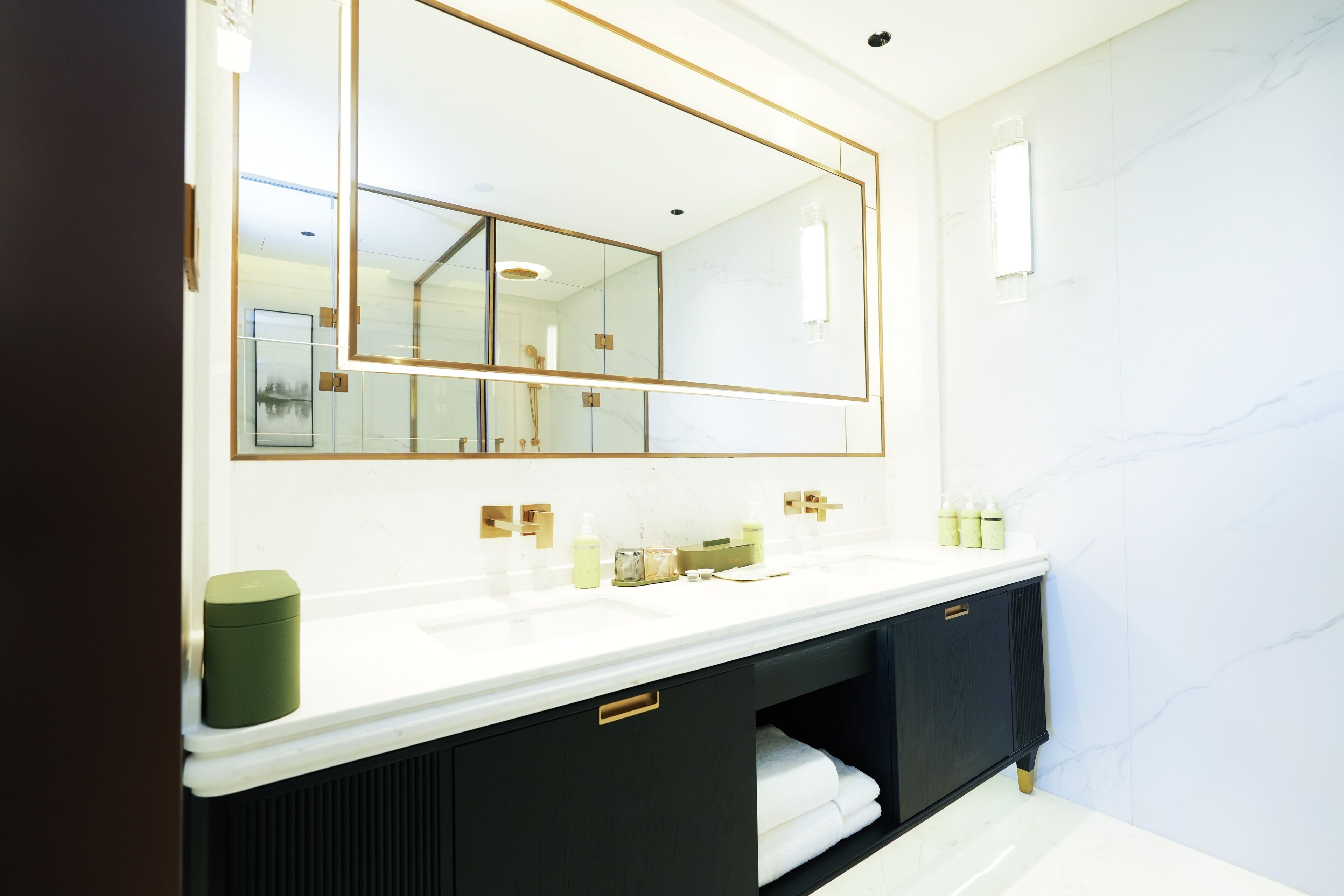 A modern bathroom with a large mirror, white marble walls, and a black vanity with gold handles.