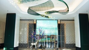 A modern lobby with a large glass wall, a decorative ceiling, and a central display featuring a metallic deer sculpture. - Chang baishan Hotel (Changchun)