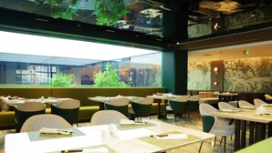 A restaurant with tables and chairs, a large window with a view, and a green wall with a mural. - Chang baishan Hotel (Changchun)