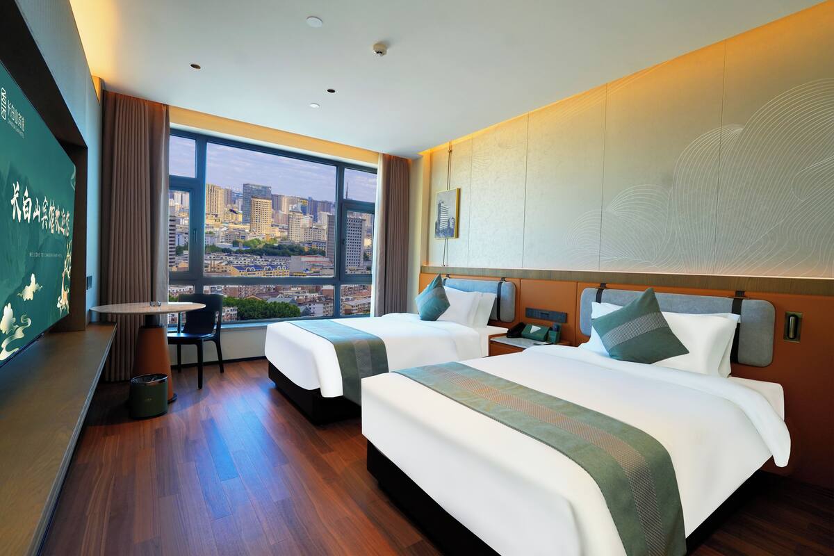 A hotel room with two beds, a dining table, and a view of the cityscape.