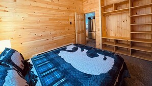 A wooden cabin room with a bed, a ceiling fan, and built-in shelves.