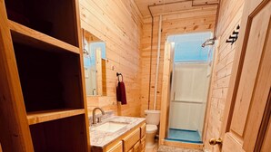A wooden cabin bathroom with a sink, toilet, and shower area.