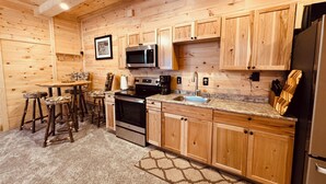 A wooden interior with a kitchen area featuring a stove, microwave, sink, and wooden cabinets.