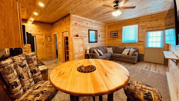 A cozy cabin interior with a round wooden table, a sofa, and a ceiling fan.