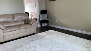 A living room with a beige leather sofa, a patterned rug, a black chair with a patterned cushion, and a wall-mounted air conditioner. - Central PEI location minutes to golf and beaches.  (Cornwall)
