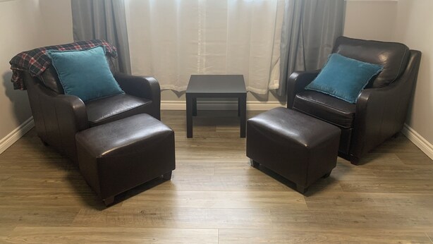 A room with two leather armchairs, a small table, and a view through sheer curtains. - Central PEI location minutes to golf and beaches.  (Cornwall)