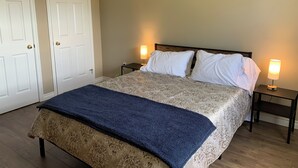 A bedroom with a bed, two bedside tables with lamps, a blue throw blanket, and two white doors. - Central PEI location minutes to golf and beaches.  (Cornwall)