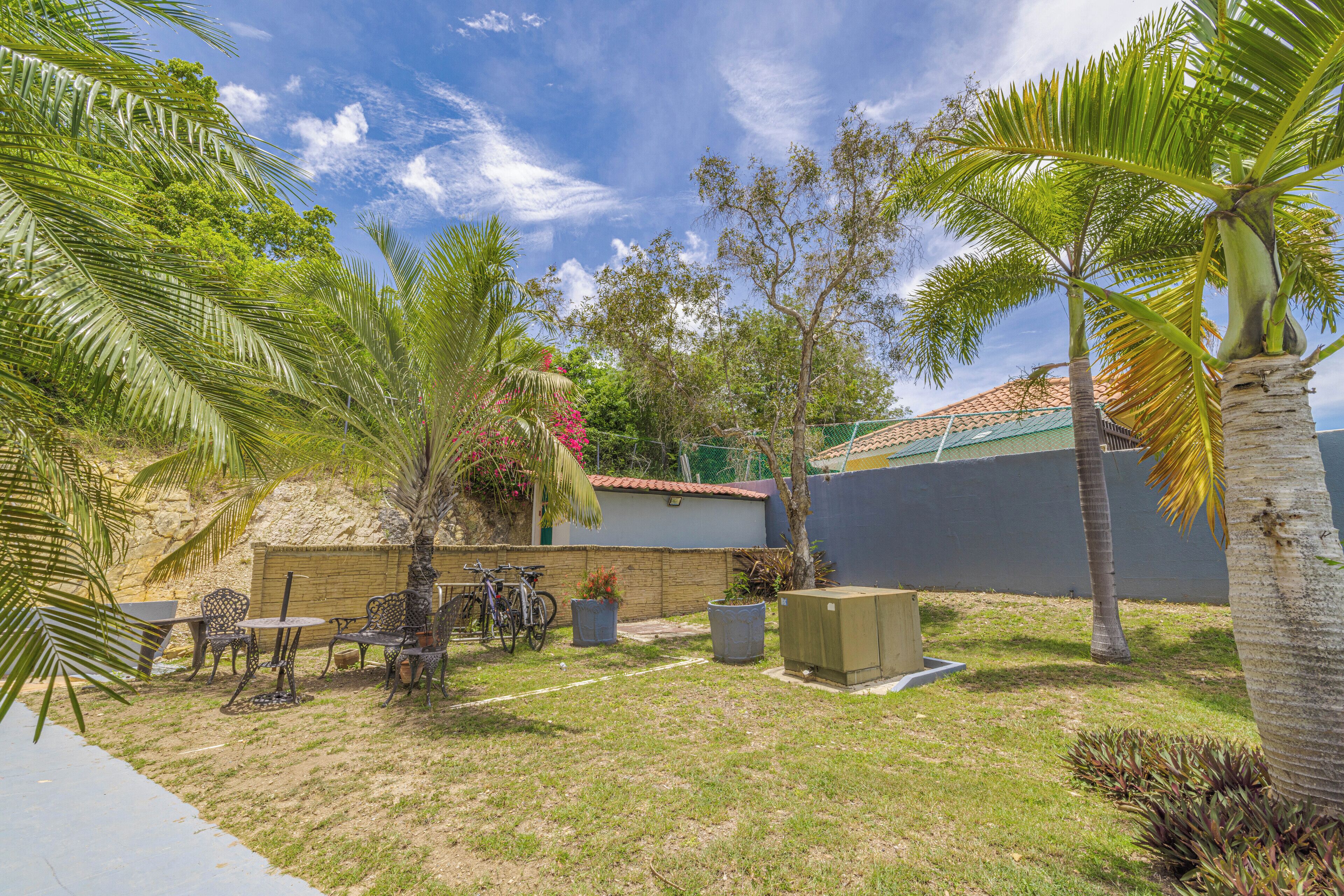 A backyard with a patio, chairs, a table, a small garden, and a fence.