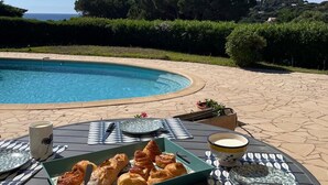 Ein Tisch am Pool mit Croissants und Kaffee, mit Blick auf einen Pool und eine schöne Aussicht auf Bäume und Hügel.