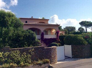 A Mediterranean-style house with a stone wall, arched windows, and a white gate.