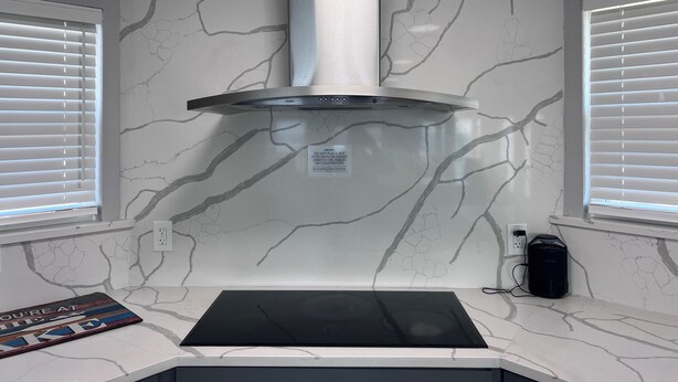 Cozinha com exaustor de aço inoxidável, backsplash de mármore branco e fogão por indução preto.