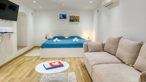 Moderni hotellihuone, jossa on sänky, sohva, televisio ja pieni pöytä.