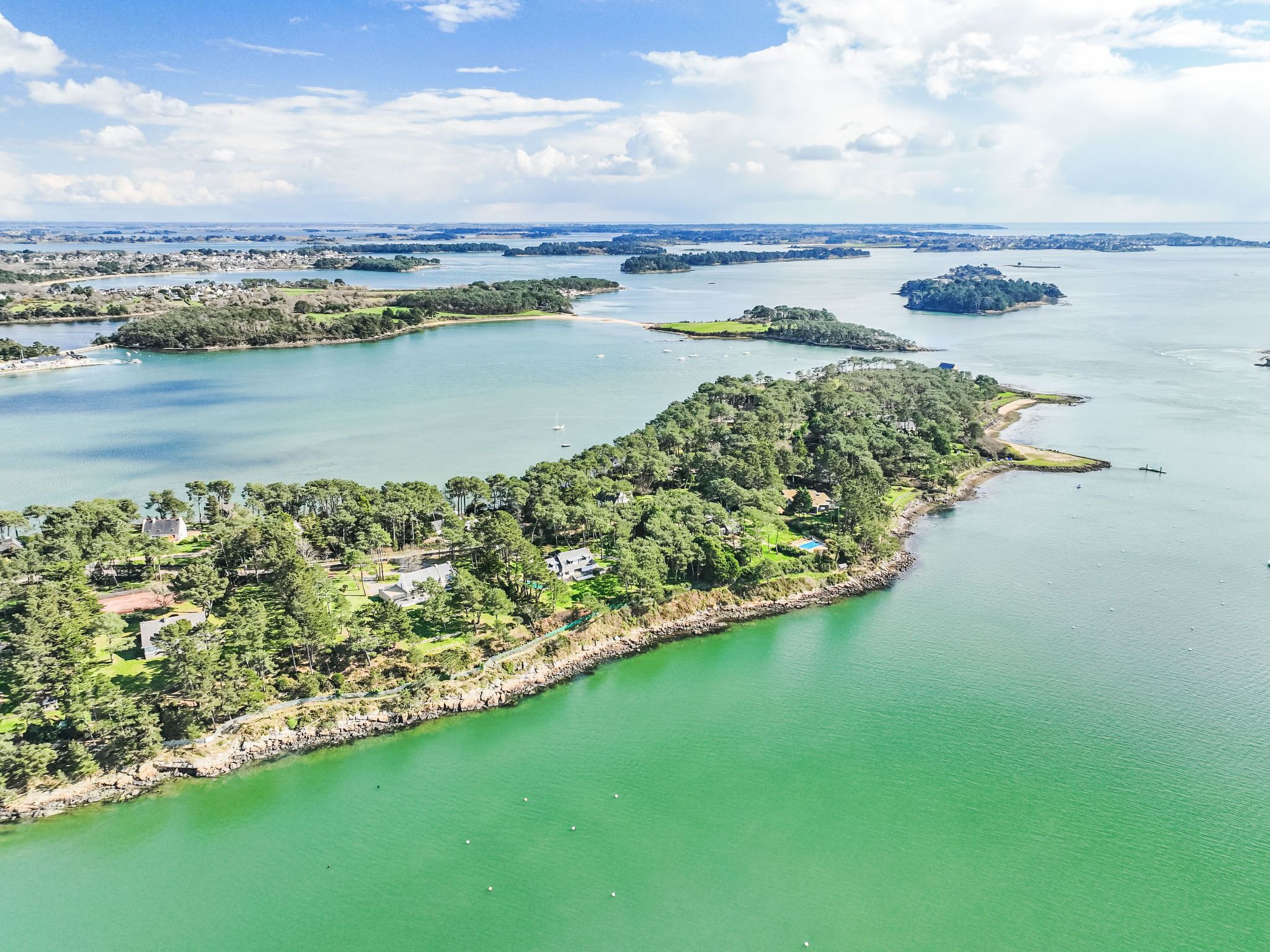 Luchtbeeld van een kustgebied met meerdere eilanden, helderblauw water en weelderige begroeiing.