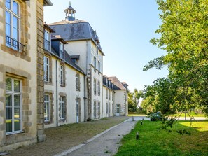 A row of historic buildings with stone facades and multiple windows, a paved pathway, and a grassy area with trees. - Le Château de Kergonano by Interhome (Baden)