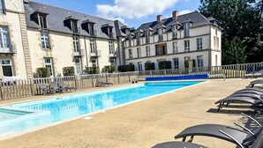 Una piscina con sillones de descanso, una valla de madera y un edificio con varias ventanas y balcones.