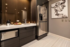 A modern kitchen with a stainless steel refrigerator, a built-in oven, and a large mirror above the countertop.