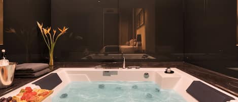 A modern bathroom with a jacuzzi tub, a fruit platter, and a vase of flowers.