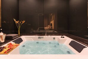 A modern bathroom with a jacuzzi tub, a fruit platter, and a vase of flowers.
