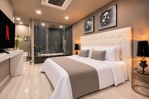 A modern hotel room with a large bed, a glass-enclosed shower, and artwork on the walls.