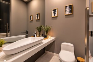 A modern bathroom with a large white bathtub, a toilet, and a sink. There are framed pictures on the wall and a small plant on the counter.
