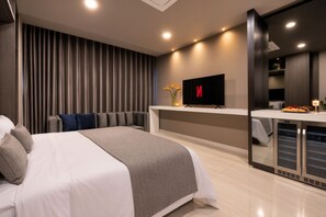 A modern hotel room with a large bed, a flat-screen TV, a minibar, and a sliding door closet.