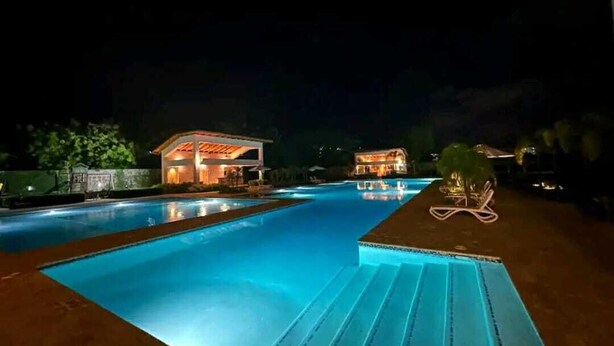 Une piscine illuminée la nuit, avec un bâtiment en arrière-plan.