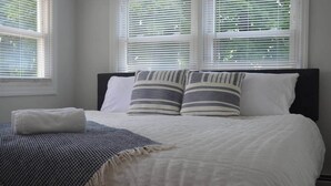 Un lit bien fait, avec des oreillers blancs et rayés, un plaid gris et une serviette blanche.