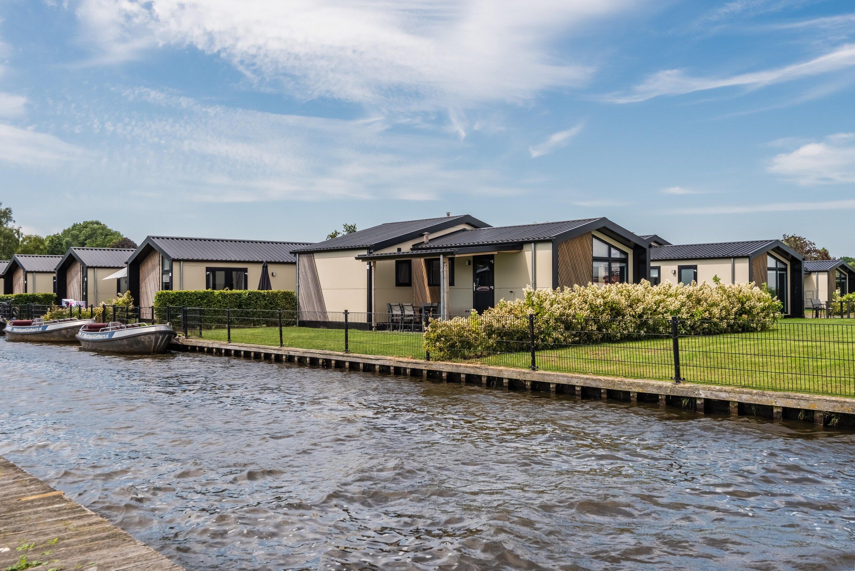 A row of modern, single-story buildings with a flat roof, situated beside a calm waterway.
