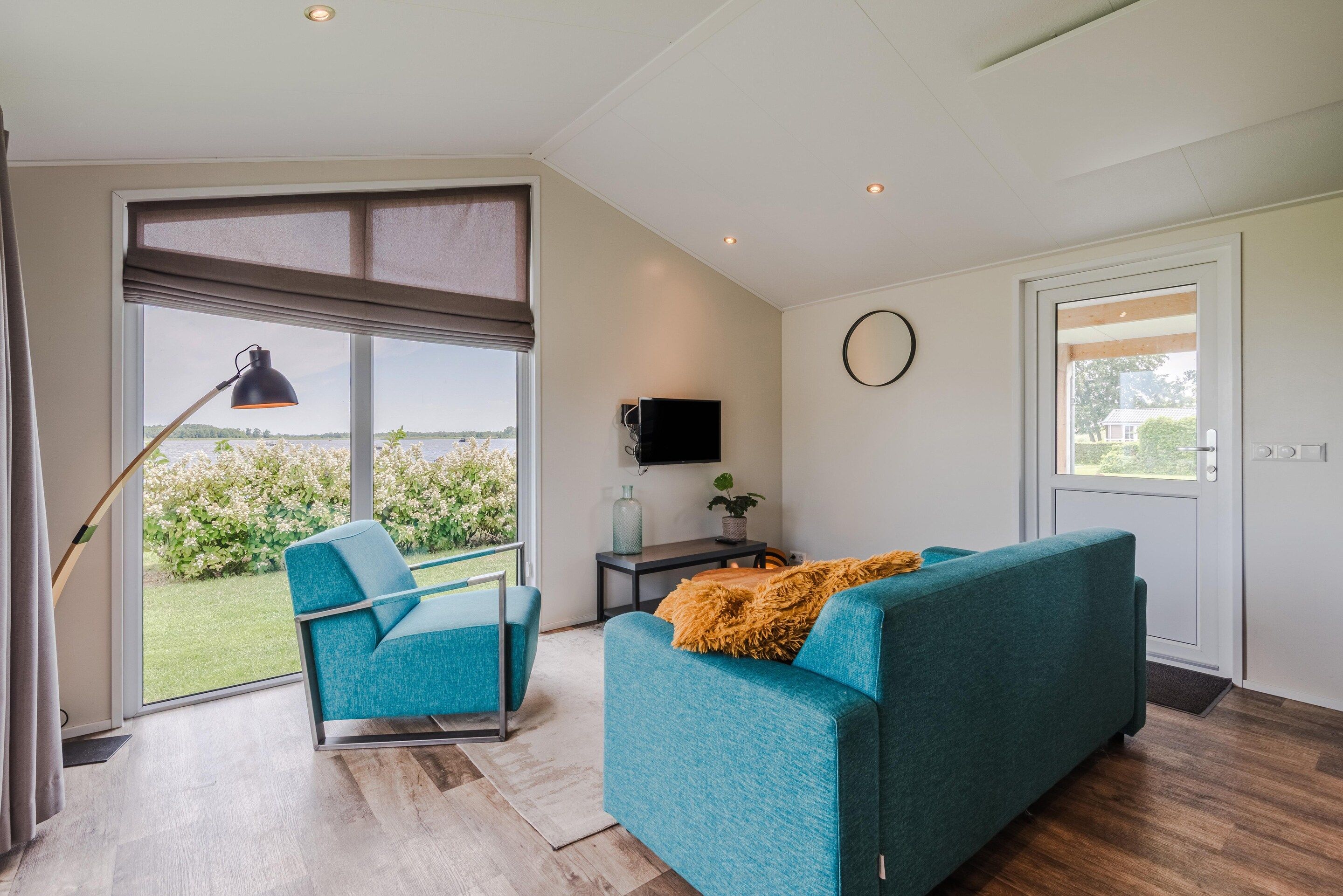 A modern living room with a sofa, a chair, a TV, and a large window offering a view of greenery.